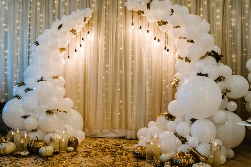 Decorated arch for wedding ceremony. White balloons, candles, autumn leaves and small pumpkins. Autumn location and Halloween decor.